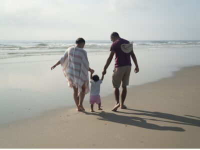 Family of two parents holding the hands of a small child walking along Wildwoods Beach in NJ