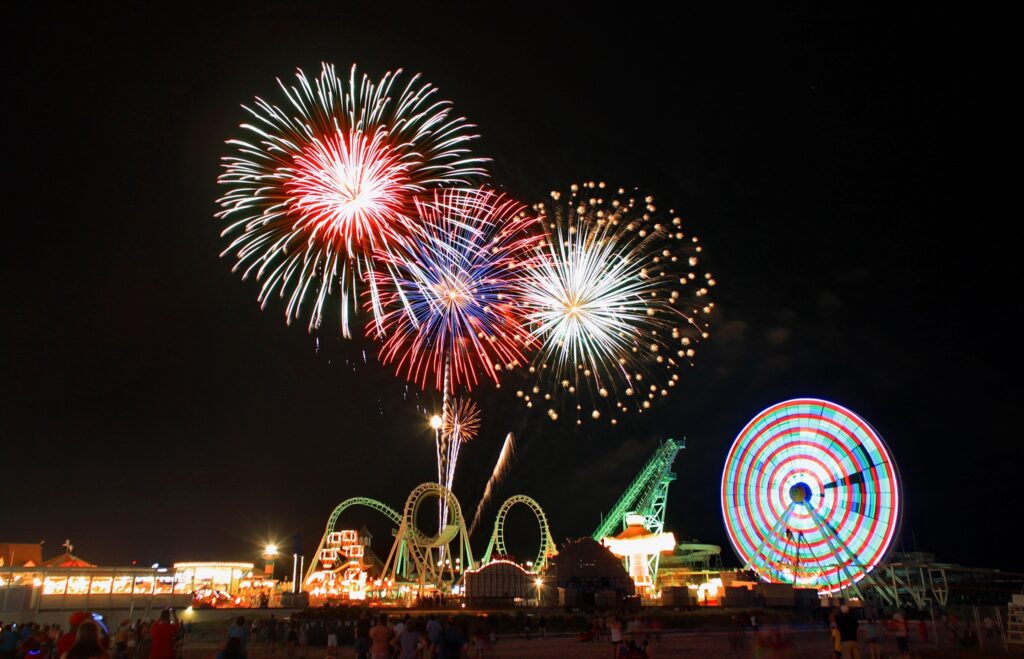 Night sky with fireworks bursting over carnival rides like ferris wheel and rollercoaster in the wildwoods NJ