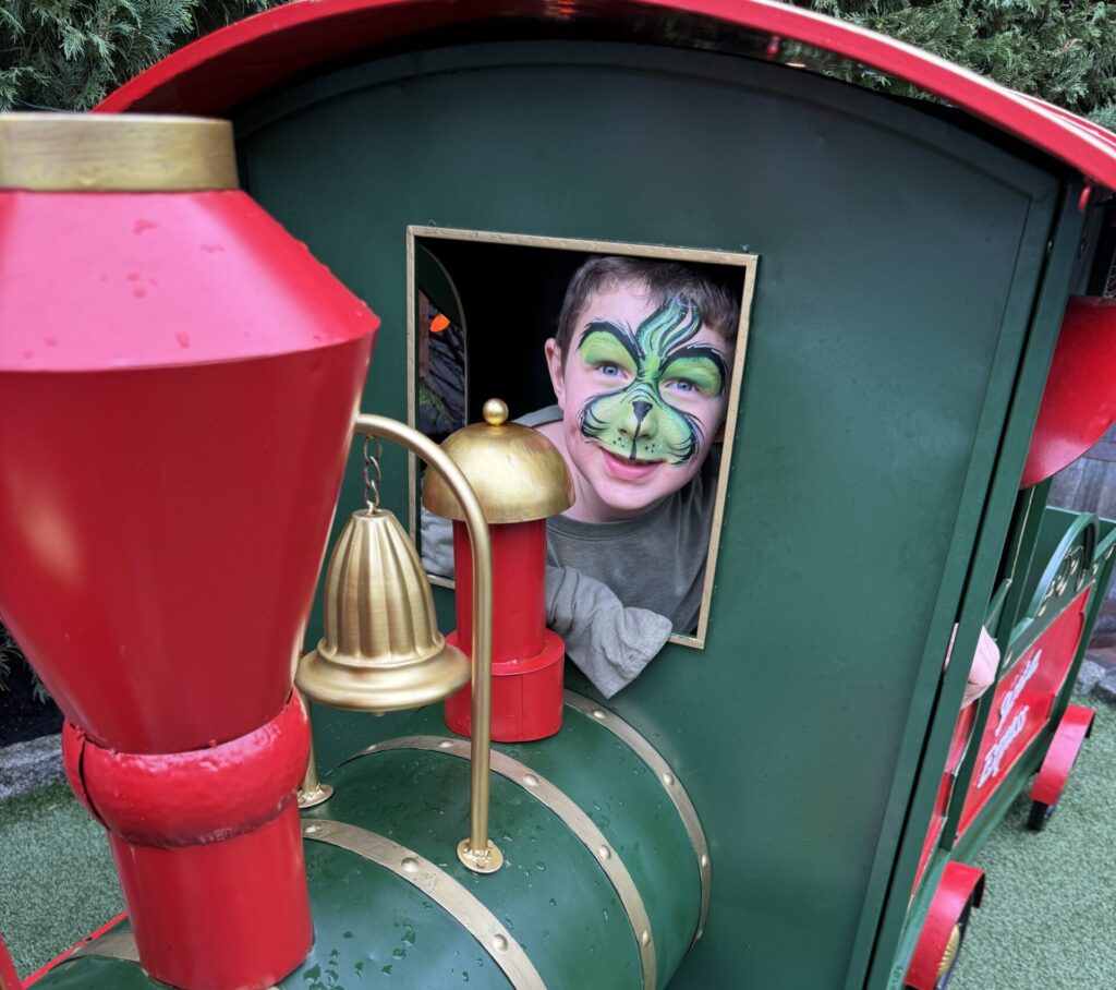 Child with Grinch face paint riding in toy train during Holidays at Henville in the Wildwoods NJ